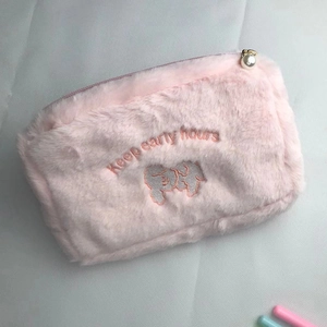 Close-up of pink plush makeup bag with embroidery and a pearl zipper pendant