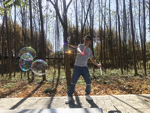 Outdoor small bubble wand creating giant colorful bubbles in a sunny forest setting
