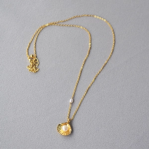 Close-up of golden shell pendant necklace with a white pearl on a grey textured background