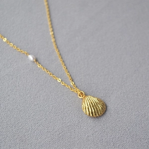 Gold shell pendant necklace with freshwater pearl accent on textured background