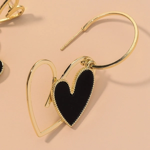 Vintage hollow gold heart earrings with black enamel detail on soft pink background