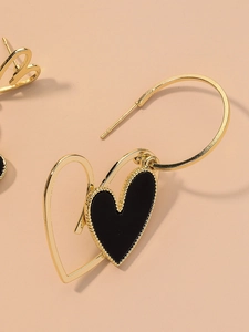 Detail view of gold hoop earrings with black and gold layered heart-shaped pendants