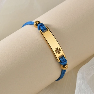 Macro view of blue braided cord bracelet with a gold rectangular clover charm detail