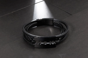 Macro detail of men's black multi-layer braided leather bracelet with steel razor blade charm
