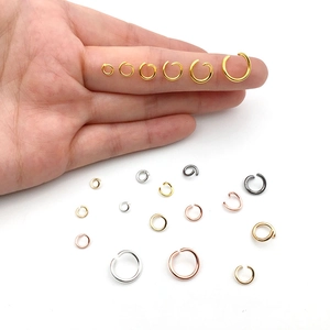 Various sizes of multi-colored metal open jump rings held by hand for DIY jewelry making