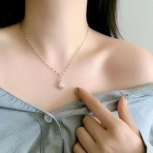 Close-up of a delicate gold chain necklace with a sparkling teardrop pendant on a model