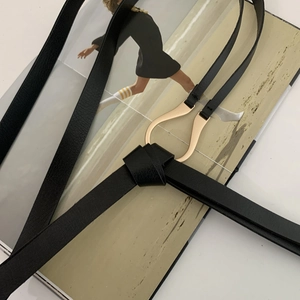 Macro detail of slim black leather belt featuring a golden horseshoe buckle with knotted style