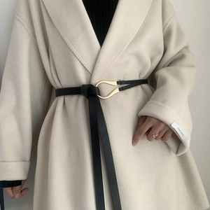 Close-up of a black leather belt with golden horseshoe buckle on a beige coat