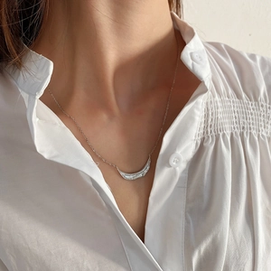 Macro detail of silver leaf texture necklace on a model wearing a white shirt