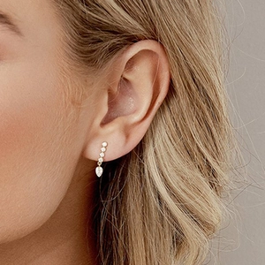 Close-up of gold drop earrings with white zircon stones on a model's ear lobe
