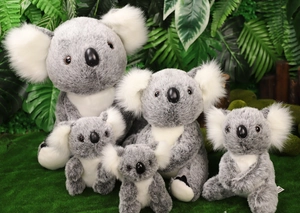 Gruppo di cinque koala di peluche in varie dimensioni su uno sfondo di piante verdi naturali