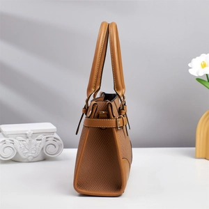 Detail view of brown patchwork handbag showing side profile and golden buckle on gray wall
