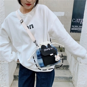 Detail of blue plaid cartoon bucket bag with a white rabbit plush keychain and drawstring