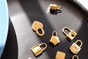 Detailed close-up of various gold-plated stainless steel lock charms on a dark tray