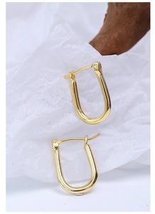 Macro detail of polished gold-plated U-shaped horseshoe earrings on minimalist background