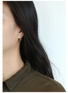 Close-up of a minimalist gold U-shaped horseshoe earring worn by a model for size