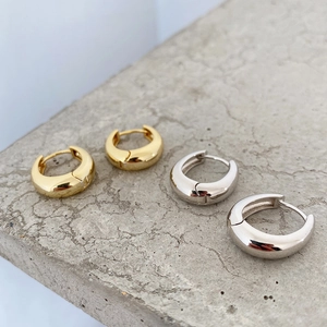 Close-up of polished gold and silver thick dome earrings on textured grey surface