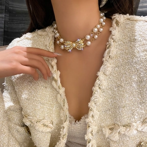 Detail of a double-layered pearl necklace with a rhinestone-studded bow pendant on a model