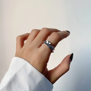 Detail of irregular wave textured silver ring worn on index finger with white shirt
