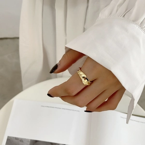 Detail of irregular hammer textured gold ring worn on finger with minimalist magazine backdrop