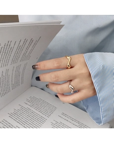 Macro detail of gold and silver irregular wave rings worn by a model holding a book