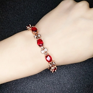 Detailed view of rose gold bracelet featuring red oval gems and clover charms on wrist