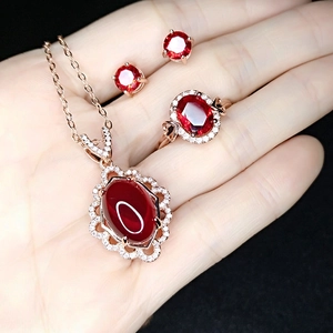 Detail of rose gold plated jewelry set with red ruby oval stones held in hand