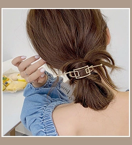 Detail of golden geometric hair pin securing a low bun with interlocking rectangles
