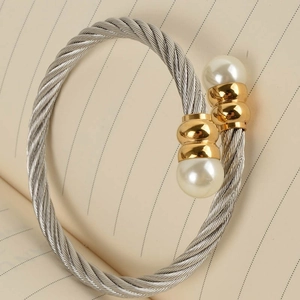 Detail of twisted cable steel bangle with golden accents and white faux pearls
