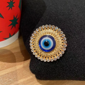 Luxury blue evil eye brooch with gold plating and sparkling crystals on black fabric