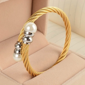 Macro detail of golden twisted wire cuff bracelet featuring elegant white pearls