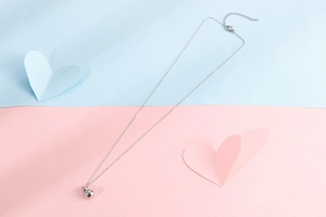 Macro shot of silver bell pendant necklace on a blue and pink decorative background