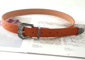 Detail of vintage carved silver buckle and metal tip on orange leather belt for women
