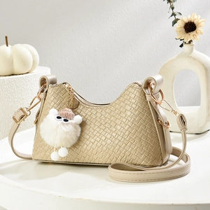 Borsa a tracolla intrecciata beige con ciondolo mostro su un tavolo decorativo bianco