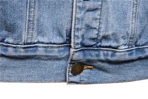 Detail of light blue denim jacket hem with metallic jeans button and contrast stitching