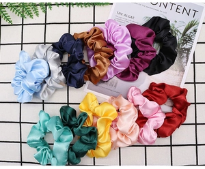 Close-up of 13 colorful satin silk scrunchies arranged on a stylish checkered background