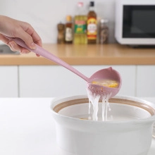 Close-up of a pink silicone soup ladle scooping food from a white ceramic cooking pot