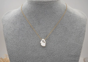 Detail of a baroque pearl pendant on a gold chain over a grey velvet bust display