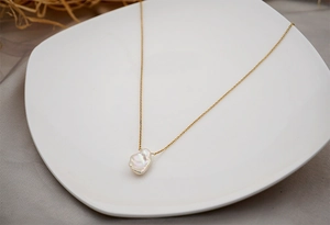 Minimalist baroque freshwater pearl necklace with a gold chain on a white ceramic tray