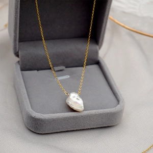 Elegant gold chain necklace with baroque pearl pendant in a grey velvet jewelry box