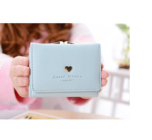 Detail of light blue tri-fold wallet with gold heart hardware held in hand
