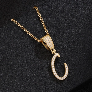 Macro shot of gold initial C pendant necklace with zircon stones on black background