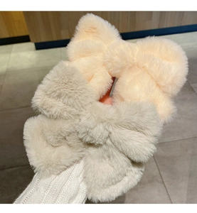 Close-up of soft plush bow hair clips in cream and grey held against a warm winter sweater