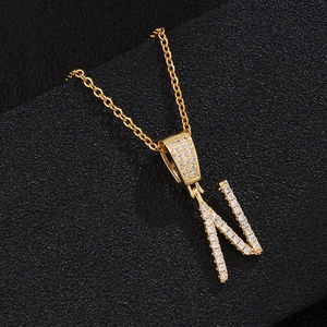 Macro detail of gold-plated letter N pendant with white zircon on black leather