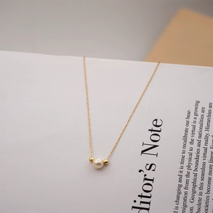 Detail of minimalist gold chain necklace with white pearl on a vintage book page