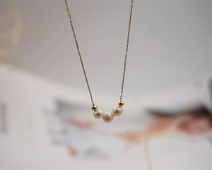 Detail of elegant gold chain necklace featuring three white pearls and small gold beads