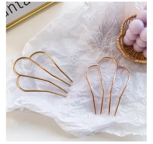 Detailed view of minimalist gold and rose gold metal hair forks on white paper
