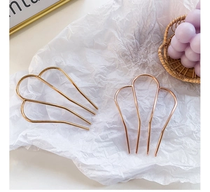 Minimalist M-shaped metal hair forks in gold and rose gold on a decorative background