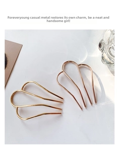 Detail of gold and rose gold U-shaped metal hair pins on white marble surface
