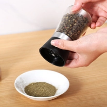 Manual black pepper grinder with clear chamber being used over a small white bowl